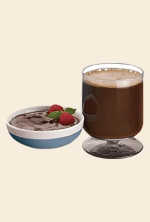 A glass of chocolate milk next to a small bowl of chocolate mousse topped with two raspberries and a sprig of mint.