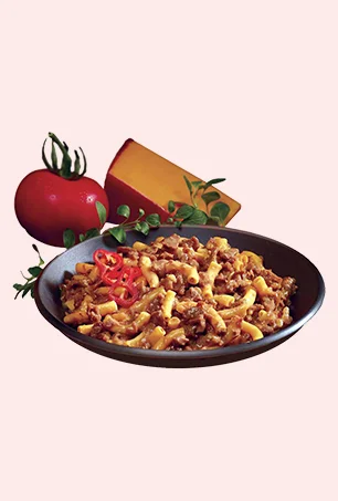 A black plate filled with macaroni mixed with ground beef and cheese, garnished with red chili slices. In the background, a tomato, a wedge of cheese, and herbs are displayed.