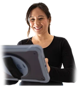 A woman with long dark hair, wearing a black top, smiles while holding and looking at a tablet device with a protective gray case.